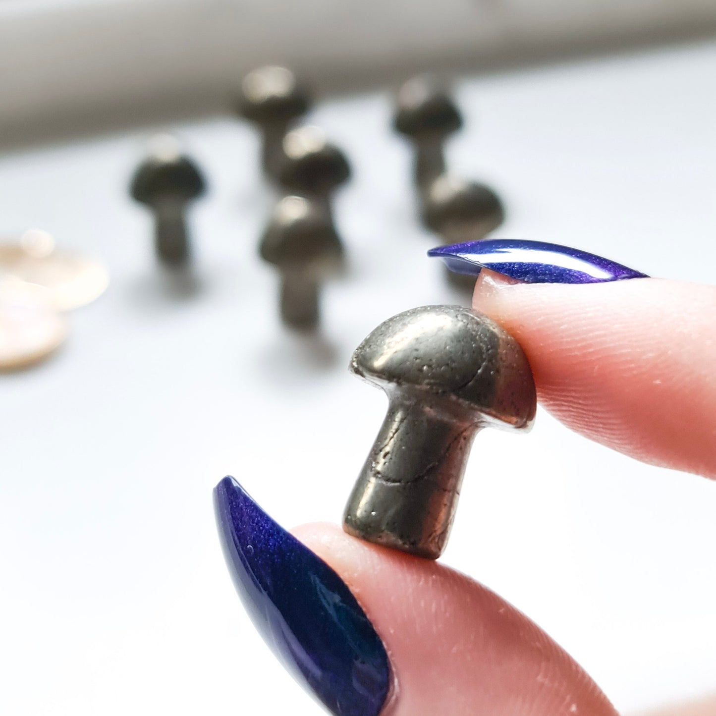 A photo of small crystal mushrooms made from pyrite, a metallic mineral that is often referred to as "fool's gold" due to its resemblance to gold. Each mushroom has a rounded cap and a short stem, and has been polished to a smooth and shiny finish. 