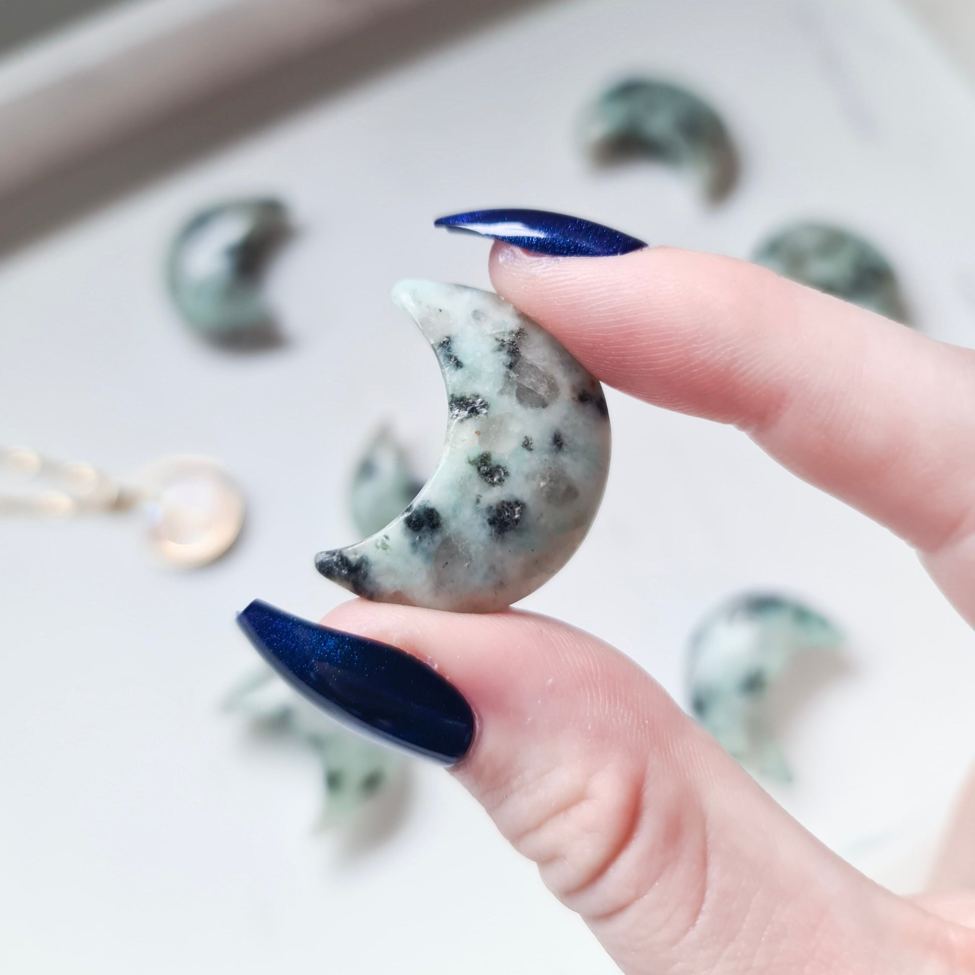 A photo of a moon carving made from kiwi jasper, a type of jasper with a greenish-yellow color and various shades of brown and black markings. The surface of the moon is polished to a smooth, shiny finish, with natural variations in texture and colour visible in the stone.