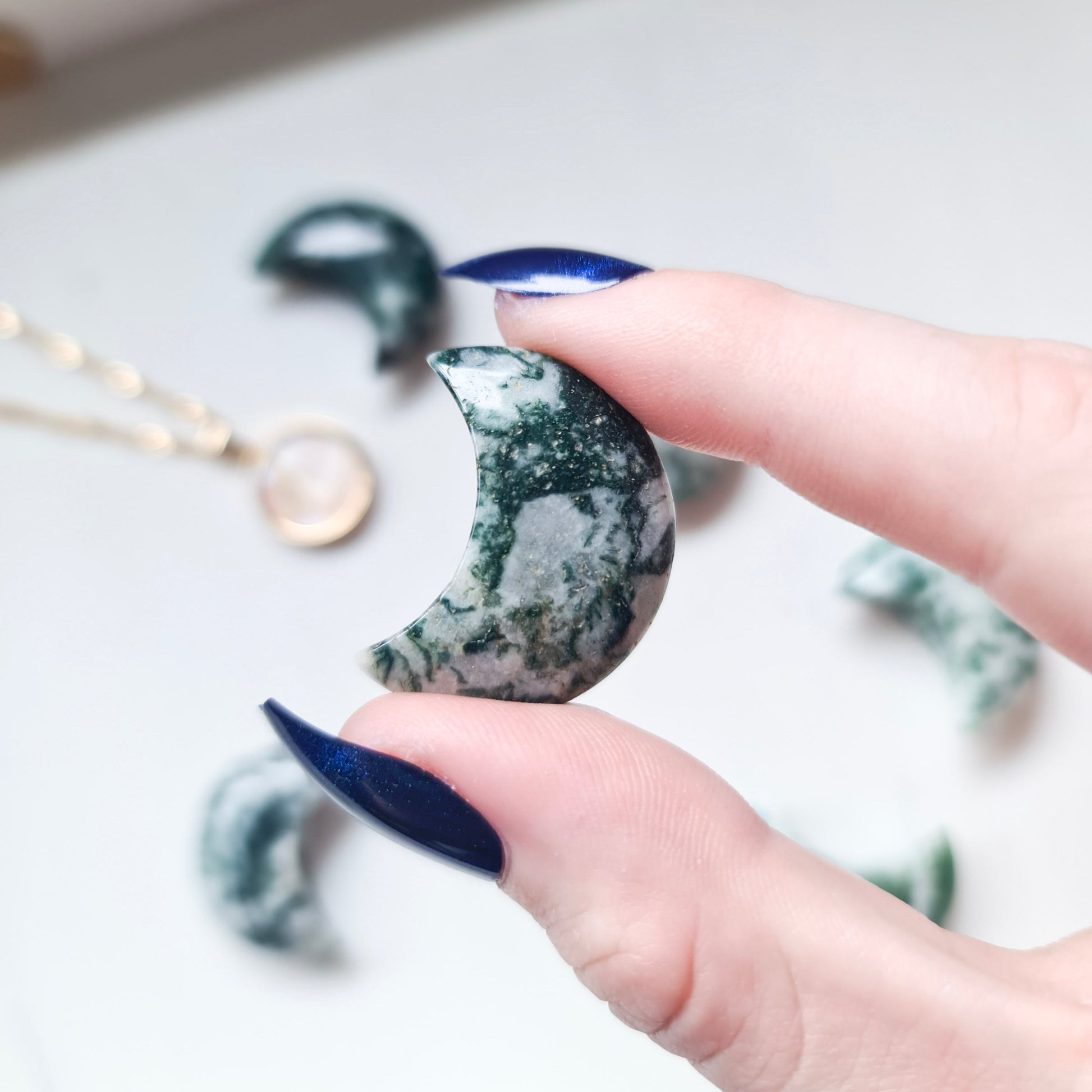 A photo of a moon carving made from tree agate, a type of agate with green and white banding that resembles the patterns of a tree. The surface of the moon is polished to a smooth, shiny finish, with natural variations in texture and colour visible in the stone. 