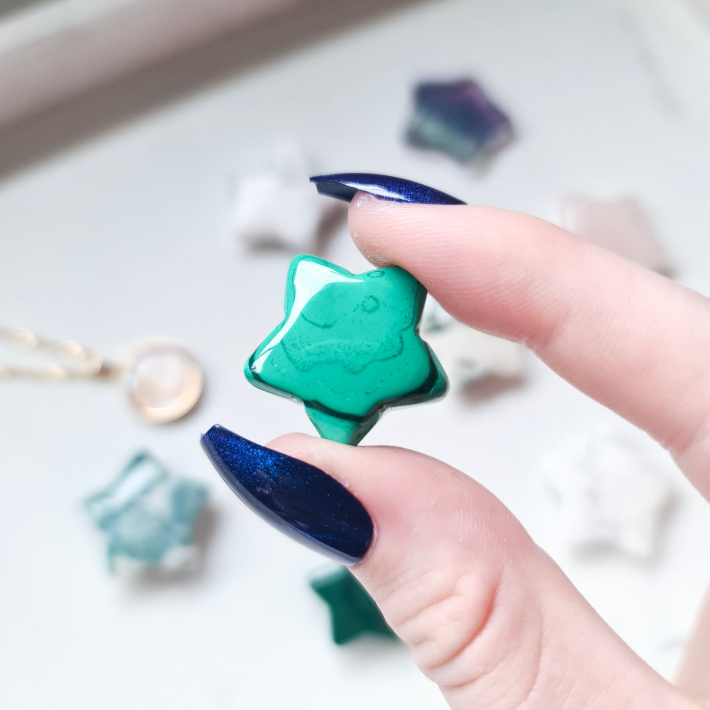 A photo of a star carving made from malachite, a green mineral with distinctive banding patterns. The surface of the star is polished to a smooth, shiny finish, with natural variations in texture and colour visible in the stone.